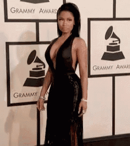 a woman in a very plunging black dress is standing in front of a wall with grammy awards logos on it .