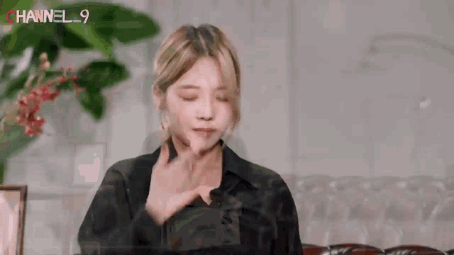 a woman in a black shirt is sitting on a couch with her eyes closed and her hands on her chest .