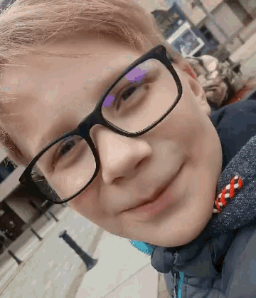 a young boy wearing glasses and a jacket is smiling