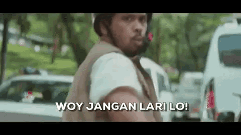 a man wearing a helmet is standing in front of a car and says woy jangan lari lo !