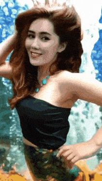 a woman in a black strapless top and green skirt is standing in front of a waterfall