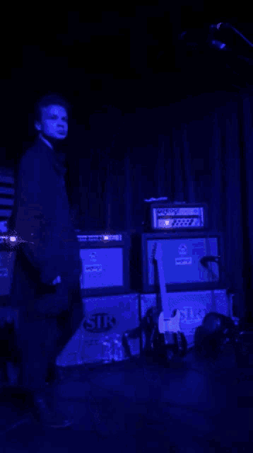 a man in a suit stands in front of a stack of orange amplifiers