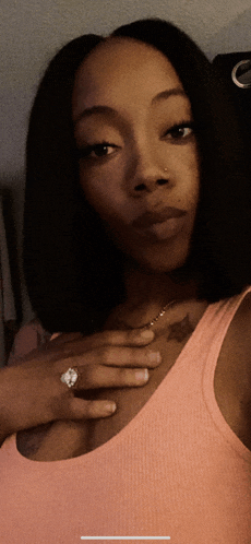 a woman in a pink tank top is taking a selfie with her hand on her chest