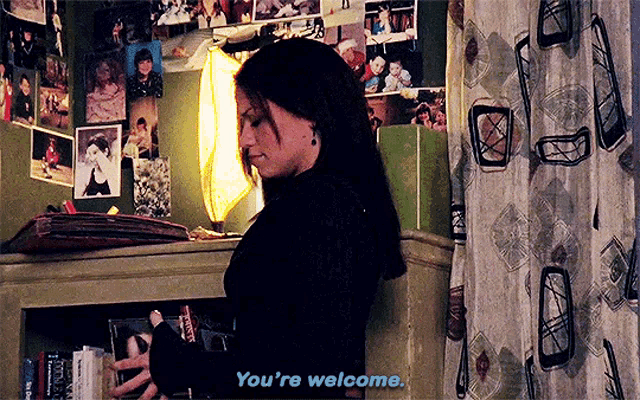 a woman is standing in front of a wall of pictures and says you 're welcome