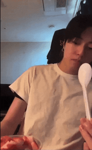 a man in a white t-shirt is holding a plastic spoon in his mouth