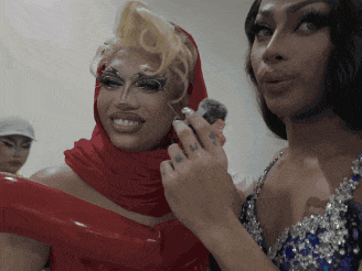 two drag queens are standing next to each other and one has a tattoo on her ring finger