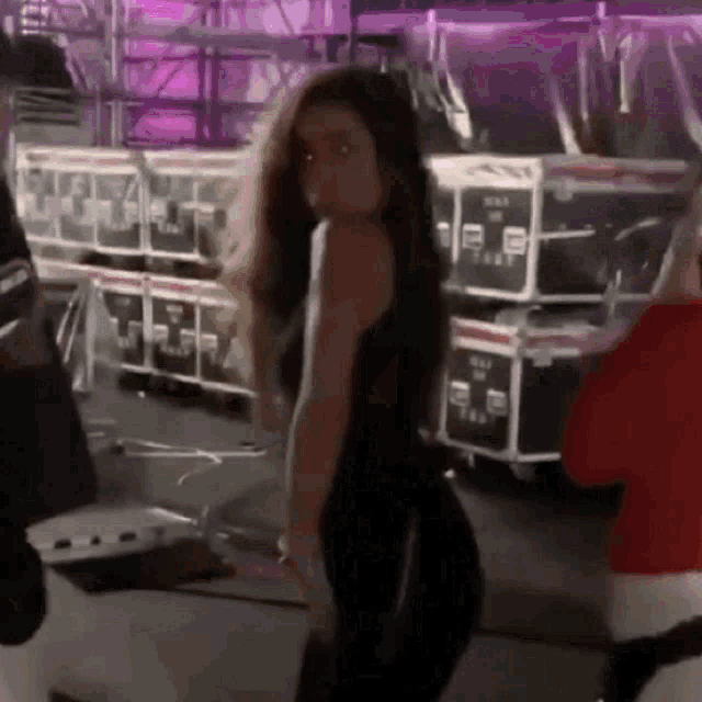 a woman in a black tank top and black pants is standing in front of a bunch of boxes .