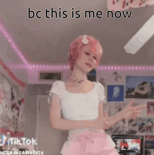 a girl with pink hair is dancing in a room with the words `` bc this is me now '' written on the ceiling .