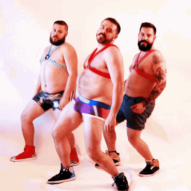 three men in underwear are dancing together and one has a tattoo on his arm
