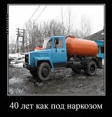 a blue truck with a large orange tank on the back is parked in a muddy lot .