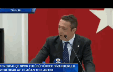 a man in a suit and tie is giving a speech in front of a flag