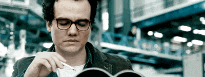 a man wearing glasses is reading a book in a library