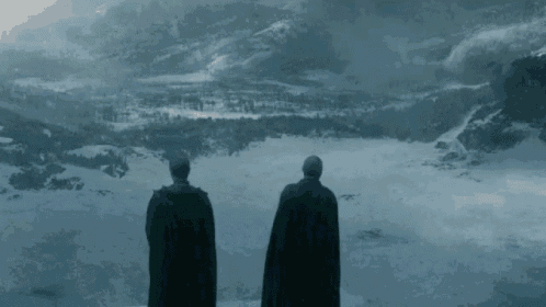 two men in capes are standing on top of a snow covered mountain .