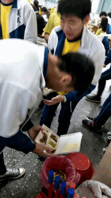 a man in a white jacket with chinese writing on the back reaches for a container of food
