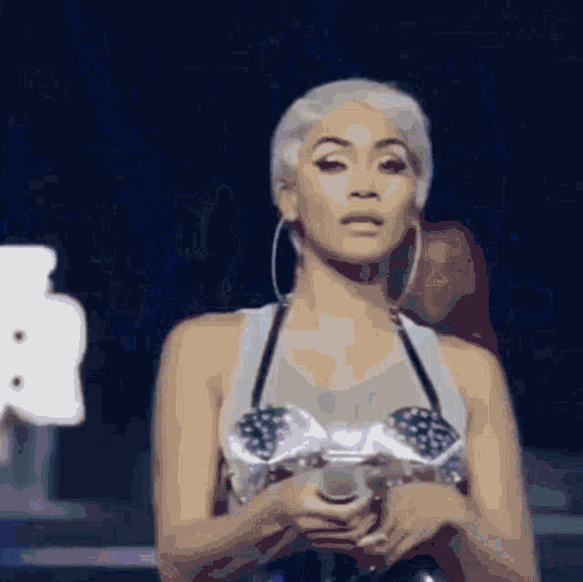 a woman in a white tank top and hoop earrings is holding a trophy
