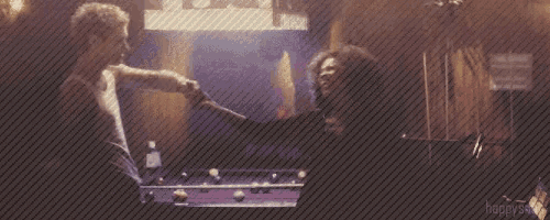 two men are playing pool in a dark room with a purple table
