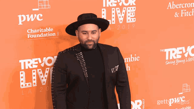 a man wearing a hat stands on a red carpet that says pwc