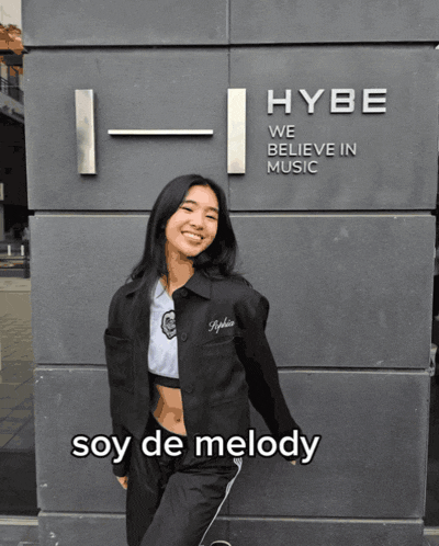 a woman stands in front of a building that says hybe