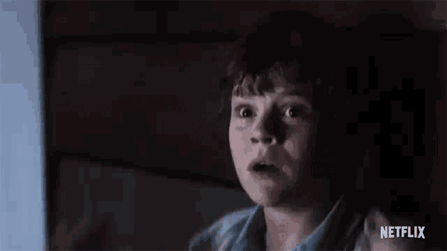 a young boy is sitting in a dark room with his mouth open and a surprised look on his face .