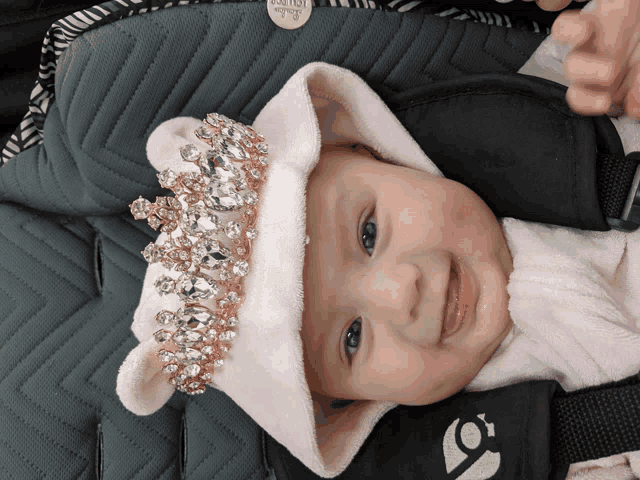 a baby wearing a pink hat with rhinestones is sitting in a stroller