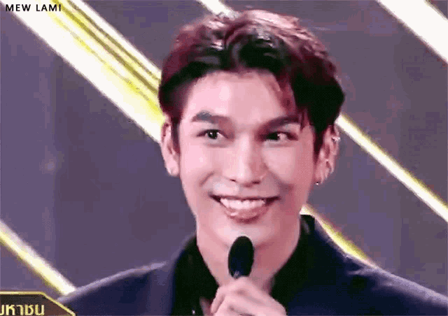 a young man is smiling while holding a microphone in front of him .