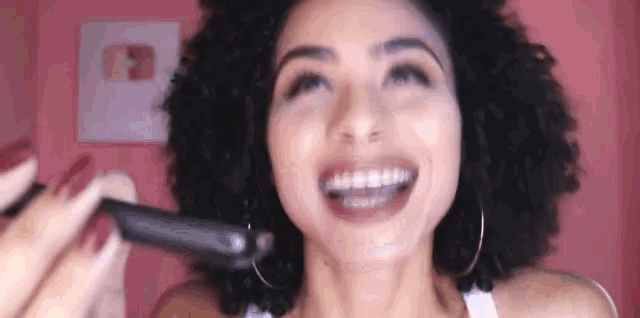 a woman with curly hair is smiling while holding a hair straightener in her hand .