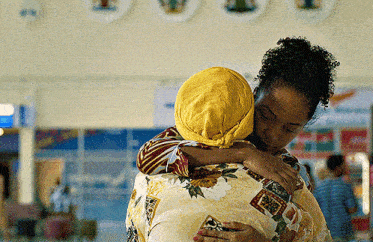 a woman in a yellow head scarf is hugging another woman in a floral shirt