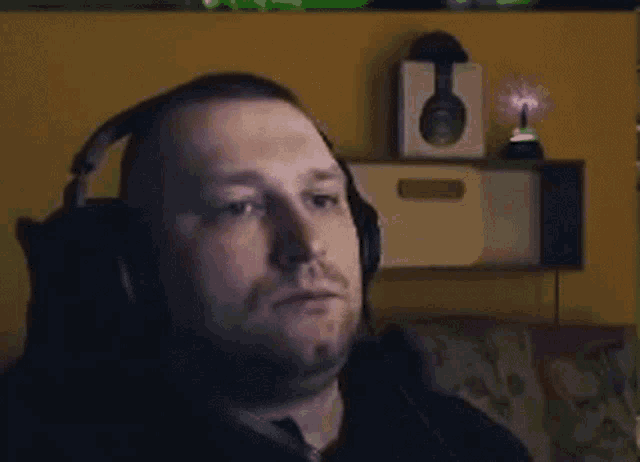 a man wearing headphones is sitting on a couch looking at the camera .