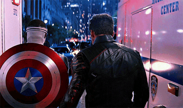 a man in a captain america shield stands next to another man in a leather jacket