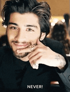 a man with a beard and a ring on his finger is smiling and holding his hand to his face .