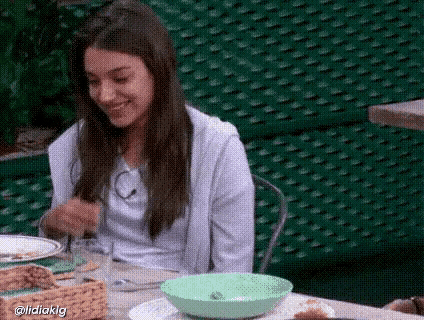 a woman is sitting at a table with a green bowl in front of her and a green fence behind her .