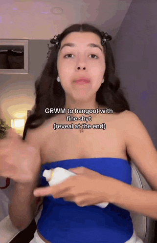 a woman in a blue top is pointing at a tube of toothpaste and says grwm to hangout with fine shyt