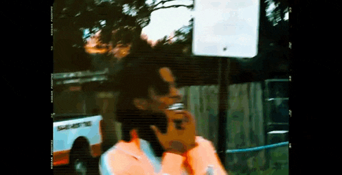 a man is smoking a cigarette while talking on a cell phone in front of a fence .