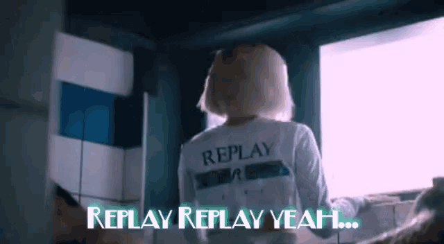 a woman wearing a white replay shirt stands in front of a window