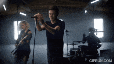a man sings into a microphone while a woman plays a guitar and a drummer plays drums