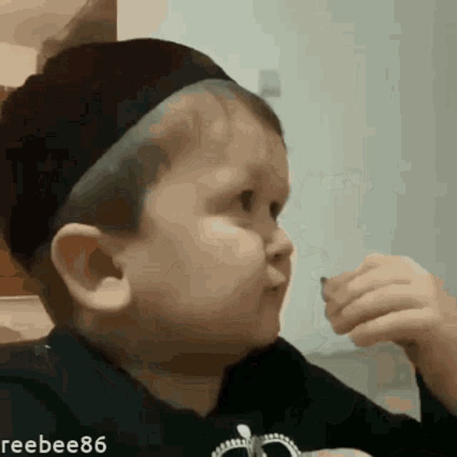 a little boy wearing a black headband is eating a piece of food .