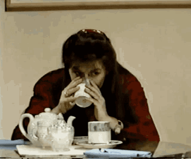 a woman sits at a table drinking a cup of tea