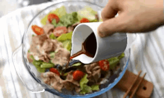 a person is pouring sauce into a bowl of food with chopsticks .