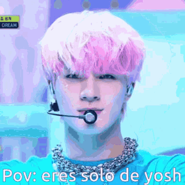 a young man with pink hair is wearing a blue shirt and a microphone .