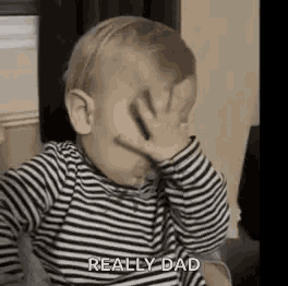 a baby is covering his face with his hand and says `` really dad '' .