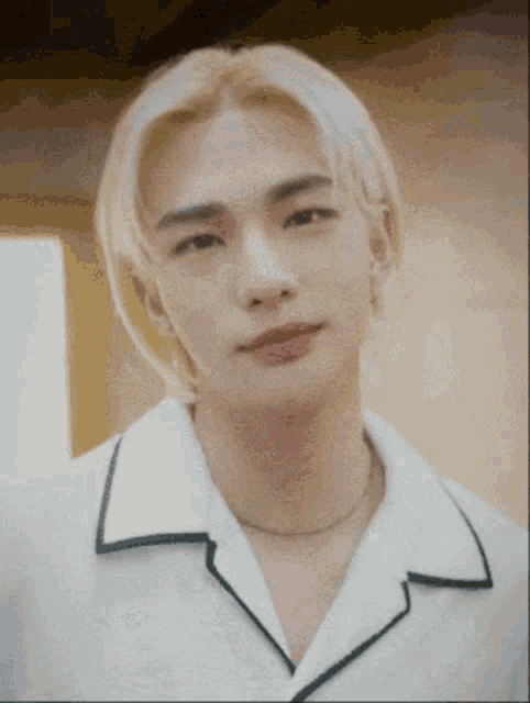 a close up of a man with blonde hair wearing a white shirt and a necklace .