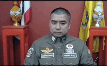 a man in a police uniform is sitting in front of a red wall with flags in the background .