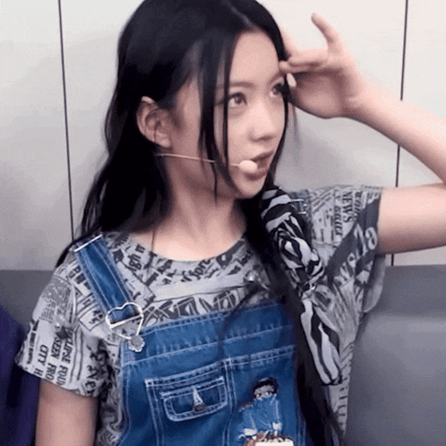 a girl wearing overalls has a microphone in her ear and a shirt with newspaper headlines on it