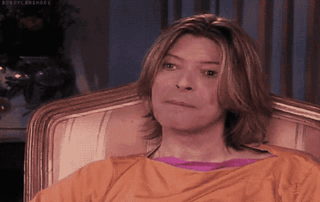 a man with long hair is sitting in a chair wearing an orange shirt and a purple shirt ..