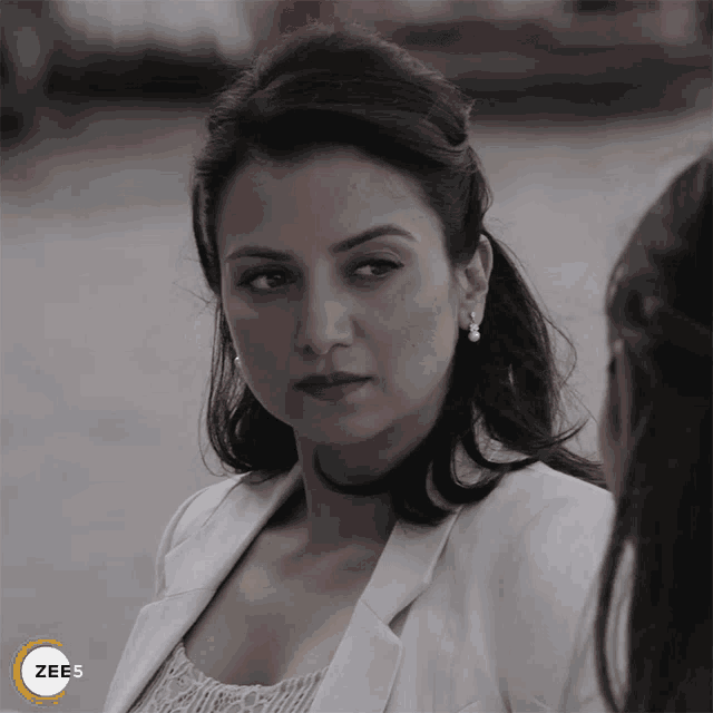 a woman in a white jacket is standing next to another woman and the word zee5 is on the bottom right