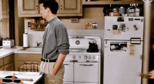 a man is standing in a kitchen with his hands in his pockets and a refrigerator .