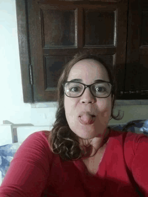 a woman wearing glasses and a red shirt sticking her tongue out