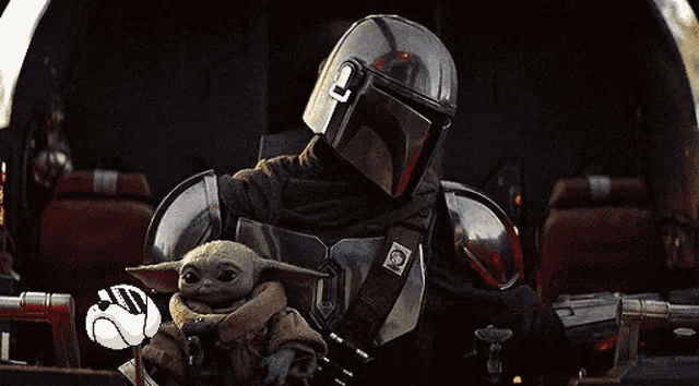 a man in a helmet is holding a baby yoda in his arms in a dark room .
