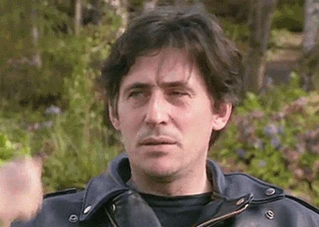 a man in a leather jacket is standing in front of a garden .
