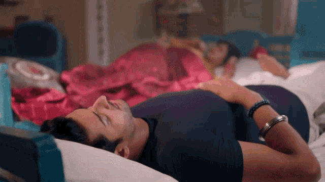 a man in a black shirt is laying on a bed with a woman in a pink blanket behind him